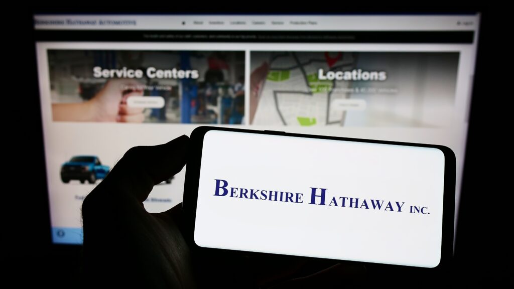  Person holding cellphone with logo of American holding company Berkshire Hathaway Inc. on screen in front of webpage. Focus on phone display. Unmodified photo.