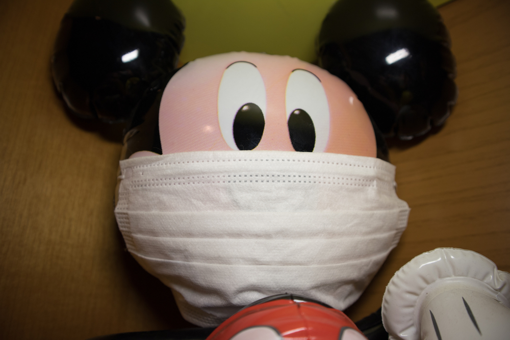 Kozani, Greece - March 2020: Face of a plastic mickey mouse with air inside. It wears a white mask. On a wooden shelf of a kids bedroom. Protection against coronavirus disease (COVID-19) outbreak.