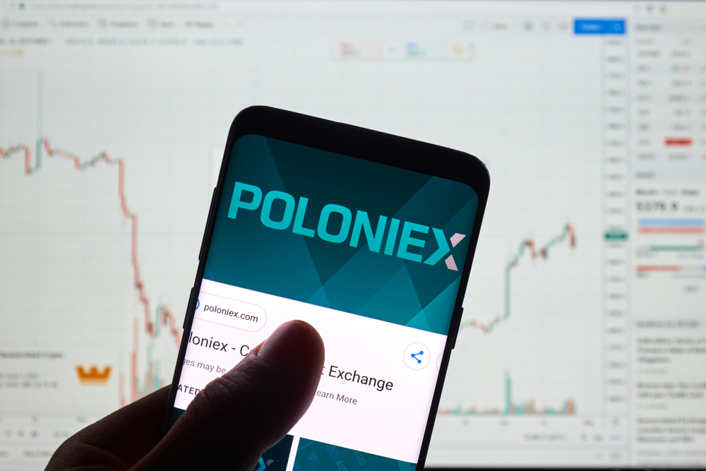 MONTREAL, CANADA - APRIL 26, 2019: Poloniex cryptocurrency exchange logo and application on Android Samsung Galaxy s9 Plus screen in a hand over a laptop display with bitcoin chart on it.